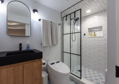 Basement bathroom featuring a black grid shower enclosure, white subway tile, and blue floral mosaic floor tile.