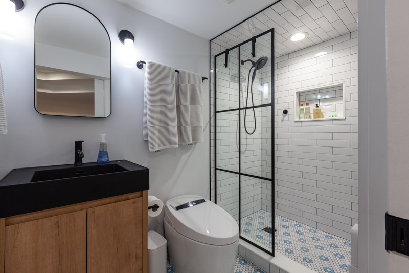 Basement bathroom featuring a black grid shower enclosure, white subway tile, and blue floral mosaic floor tile.