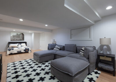 Open-concept finished basement with light oak flooring, media lounge, and integrated guest bed nook.