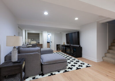 Open-concept finished basement with light oak flooring, media lounge, and integrated guest bed nook.