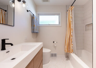Bright main-floor hall bathroom remodel with terrazzo floor tiles, white arch shower tile, and matte black fixtures.