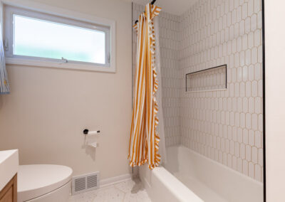 Bright main-floor hall bathroom remodel with terrazzo floor tiles, white arch shower tile, and matte black fixtures.