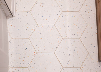 Bright main-floor hall bathroom remodel with terrazzo floor tiles, white arch shower tile, and matte black fixtures.