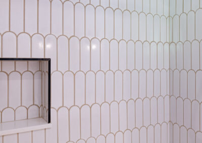 Bright main-floor hall bathroom remodel with terrazzo floor tiles, white arch shower tile, and matte black fixtures.