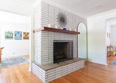 Modern mid-century white stacked brick fireplace with a floating wood mantel and starburst clock in a La Grange home.