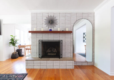 Modern mid-century white stacked brick fireplace with a floating wood mantel and starburst clock in a La Grange home.