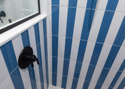 Modern primary bathroom featuring bold blue and white vertical striped tile, wall-mounted faucet, and oak vanity.